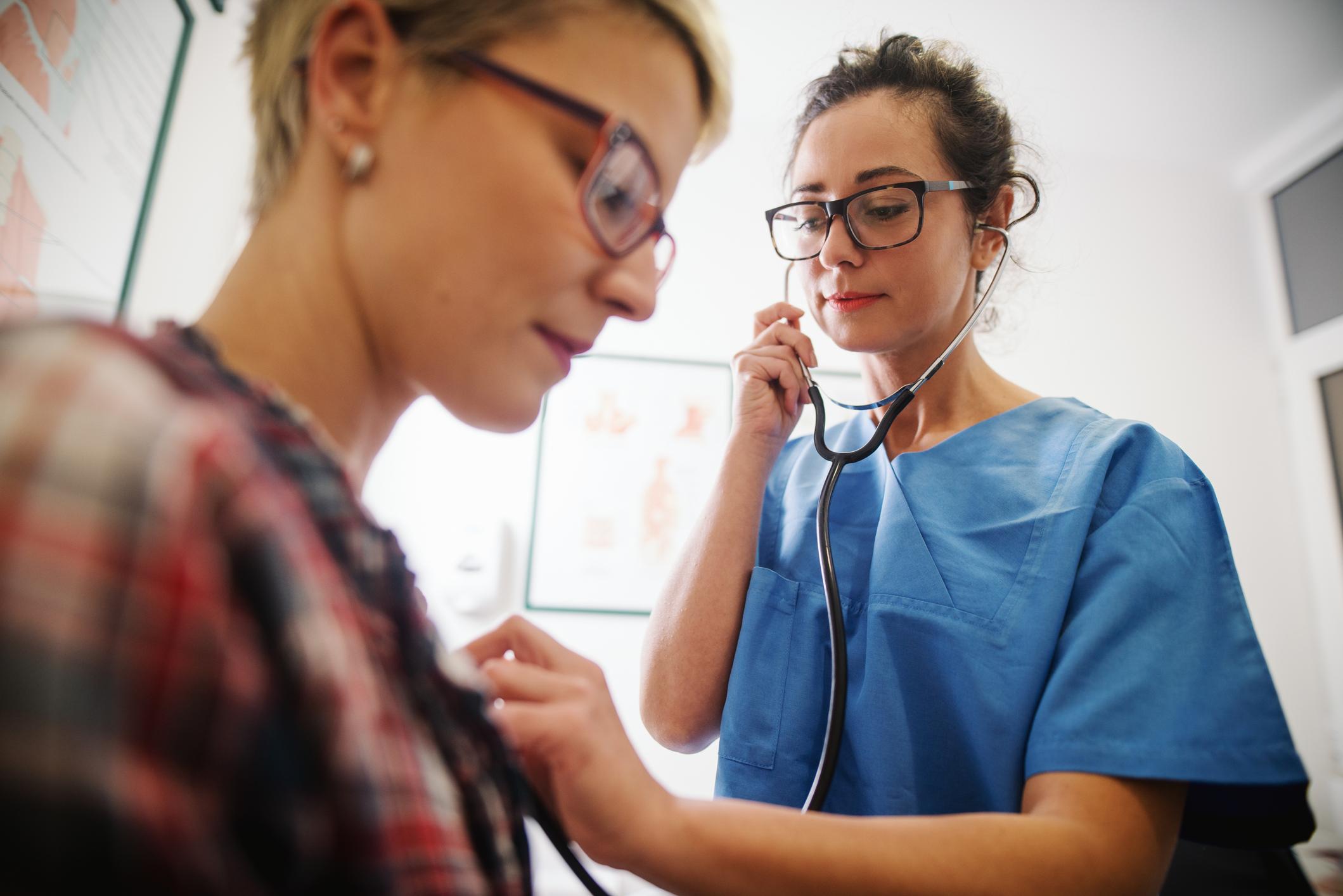 Female middle-aged nurse using stethoscope to examine patient.