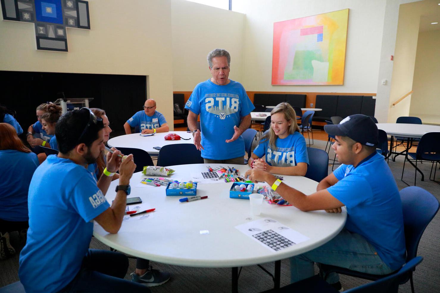 president danko addressing table of males and females, all in light blue t-shirts that read BITS